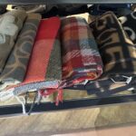 さまざまなデザイン素材の冬用マフラーが並んでいる様子。起毛タイプや柄入りの大判ストールなど、複数の種類がまとまって陳列されている。