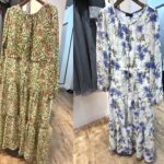 ハニーサックル柄のグリーンワンピースと、青ゆり柄の白ベースワンピースが店内に並んで掛けられている様子