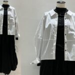 白のコットン素材で立体タックが入ったボトルシルエットのブラウスを、黒のインナーとロングスカートに合わせたコーディネート。