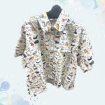 カラフルなねこのイラストが全面に描かれた、アイボリーカラーの半袖総柄シャツ